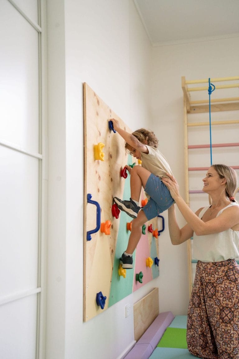 A mother and child climbing on a wall in a playroom.
